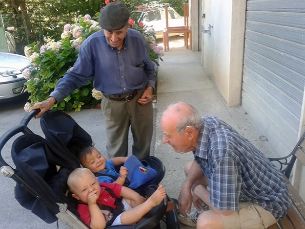 two older man play with two babies in a tandem stroller