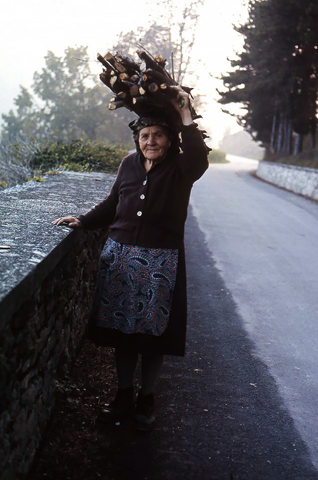 an old Italian woman carries a bundle of sticks on her head